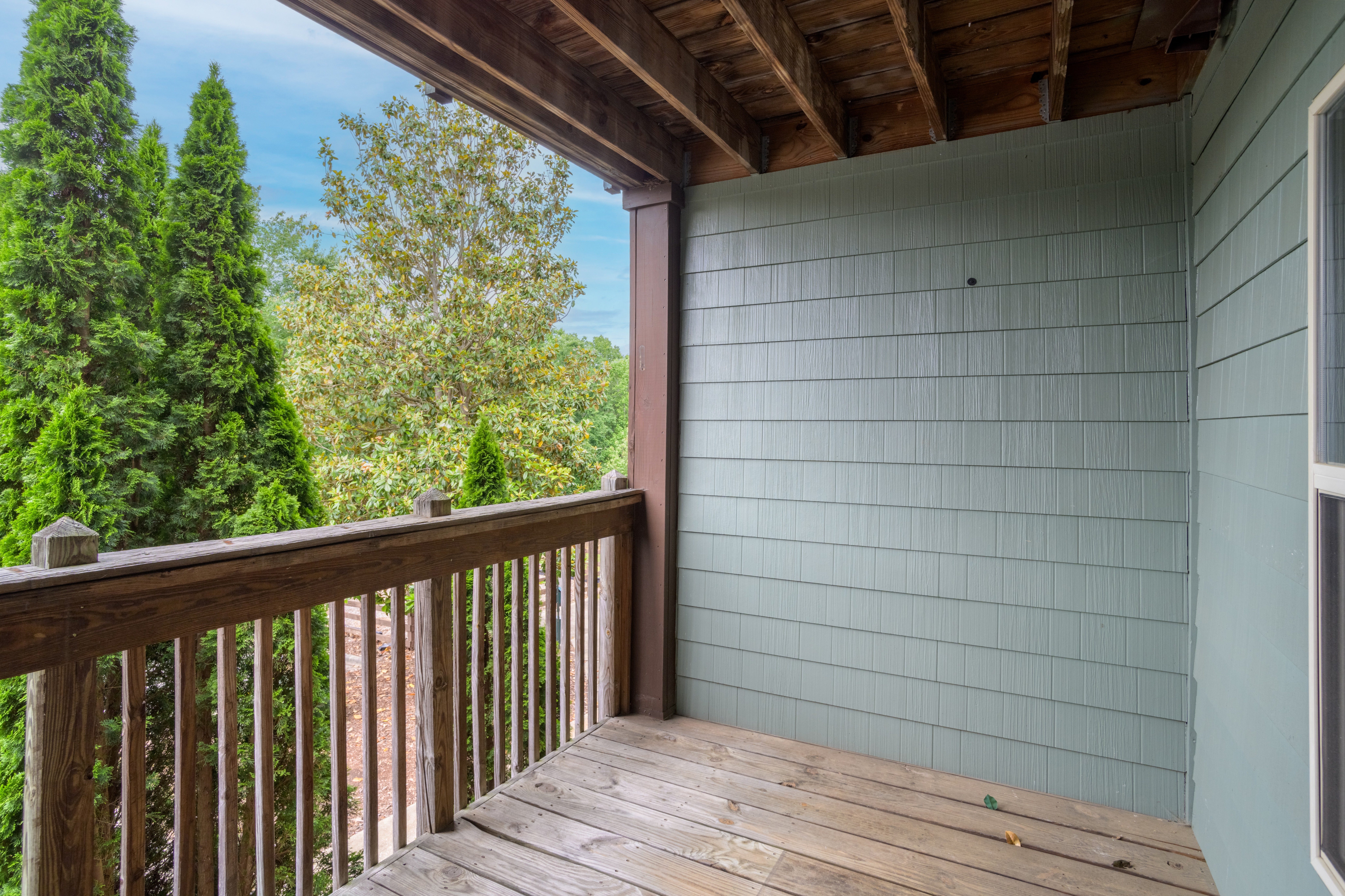 A wooden deck with a railing and a view of trees.,A wooden deck with a railing and a view of trees.